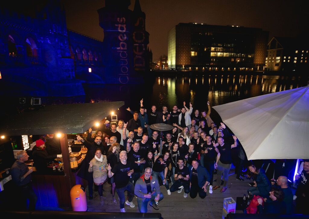 Overhead group photograph of IDeaS and Cloudbeds party attendees with blue Oberbaum bridge in background